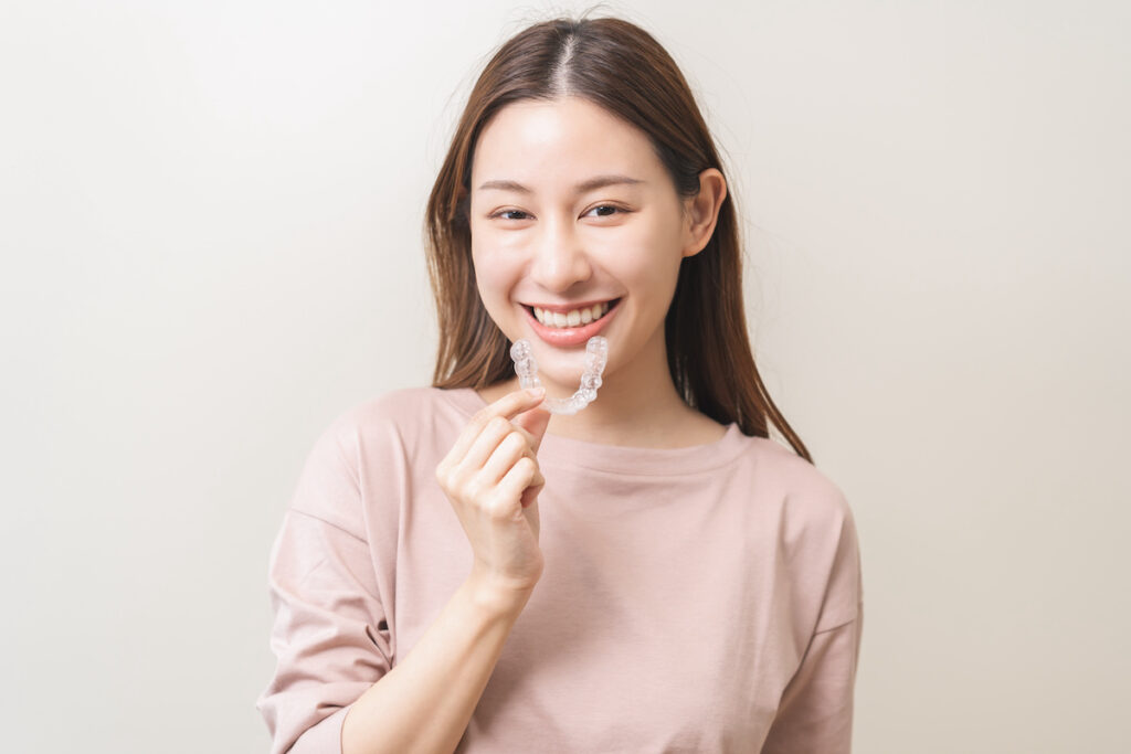Dental invisible braces, beautiful smiling asian young woman holding invisalign braces, wearing orthodontic silicone trainer, white smile using invisible whitening tray. Stomatology, dental healthcare